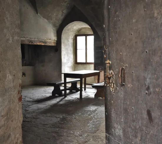 Mittelalterlicher Steinraum mit Holztisch und Bänken neben gewölbtem Fenster